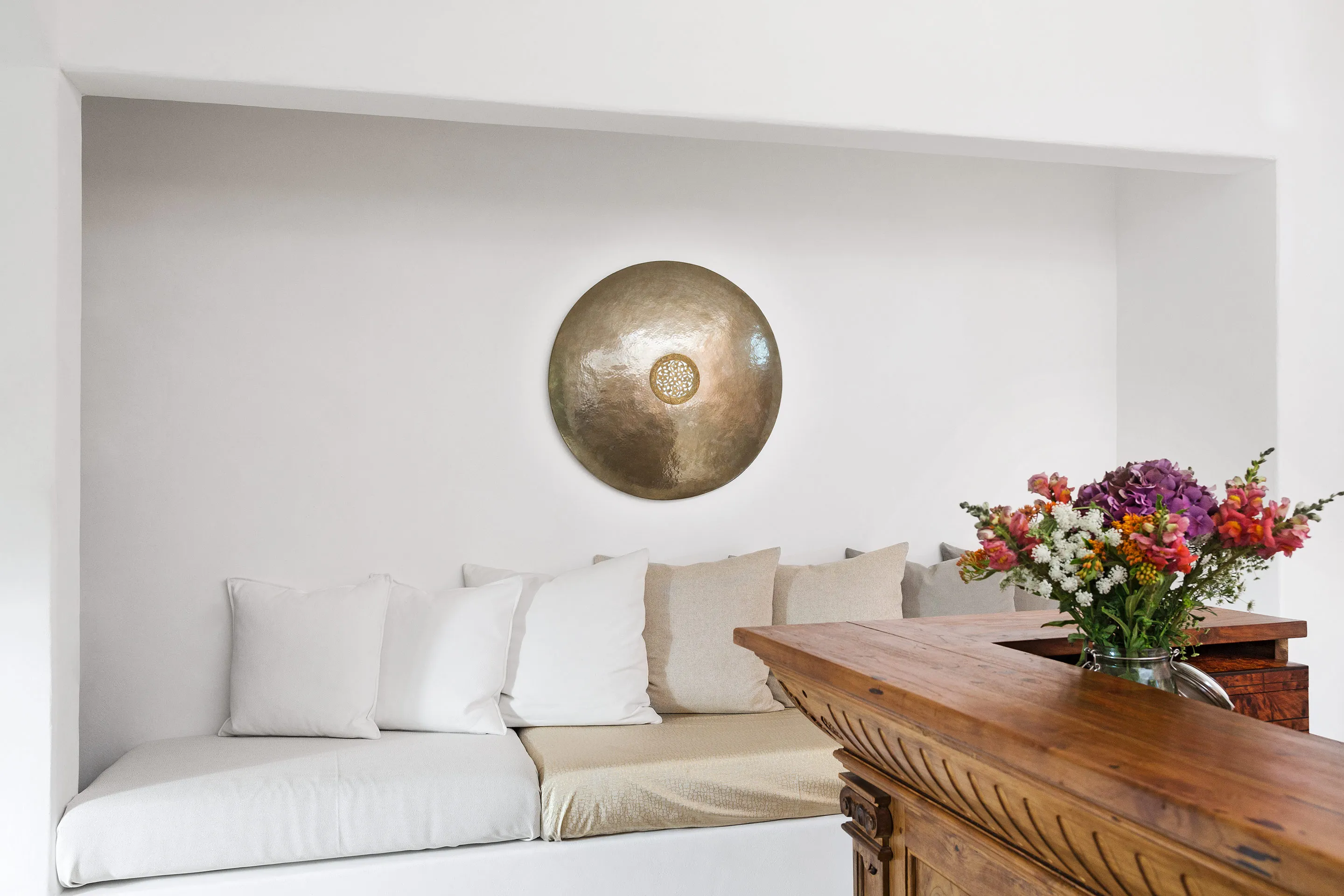 Heller Salon der Villa mit Leinensofa, Messing-Wandobjekt und frischen Blumen